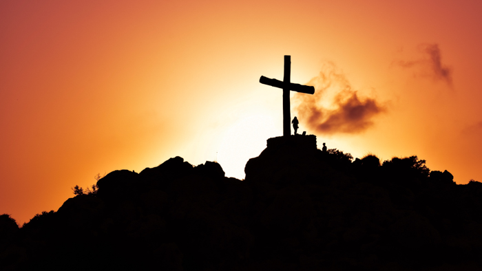 Foto legal da silhueta de uma garota ao lado de uma cruz gigante em uma montanha ao pôr do sol