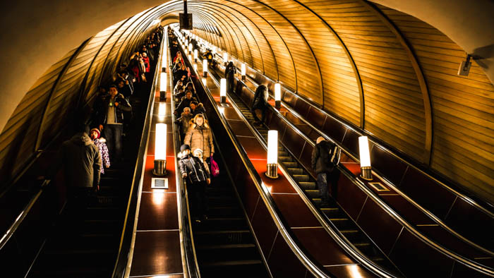 A profunda estação de metrô está cheia de pessoas nas escadas rolantes