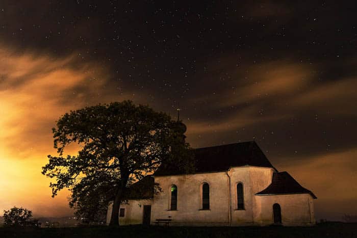 Fotografia noturna de longa exposição de uma pequena igreja e uma árvore sob o céu noturno