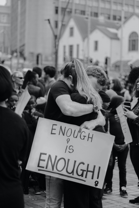 imagem em preto e branco de duas pessoas se abraçando durante um protesto 