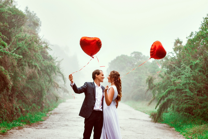 Uma foto de um casal elegante segurando balões em forma de coração.